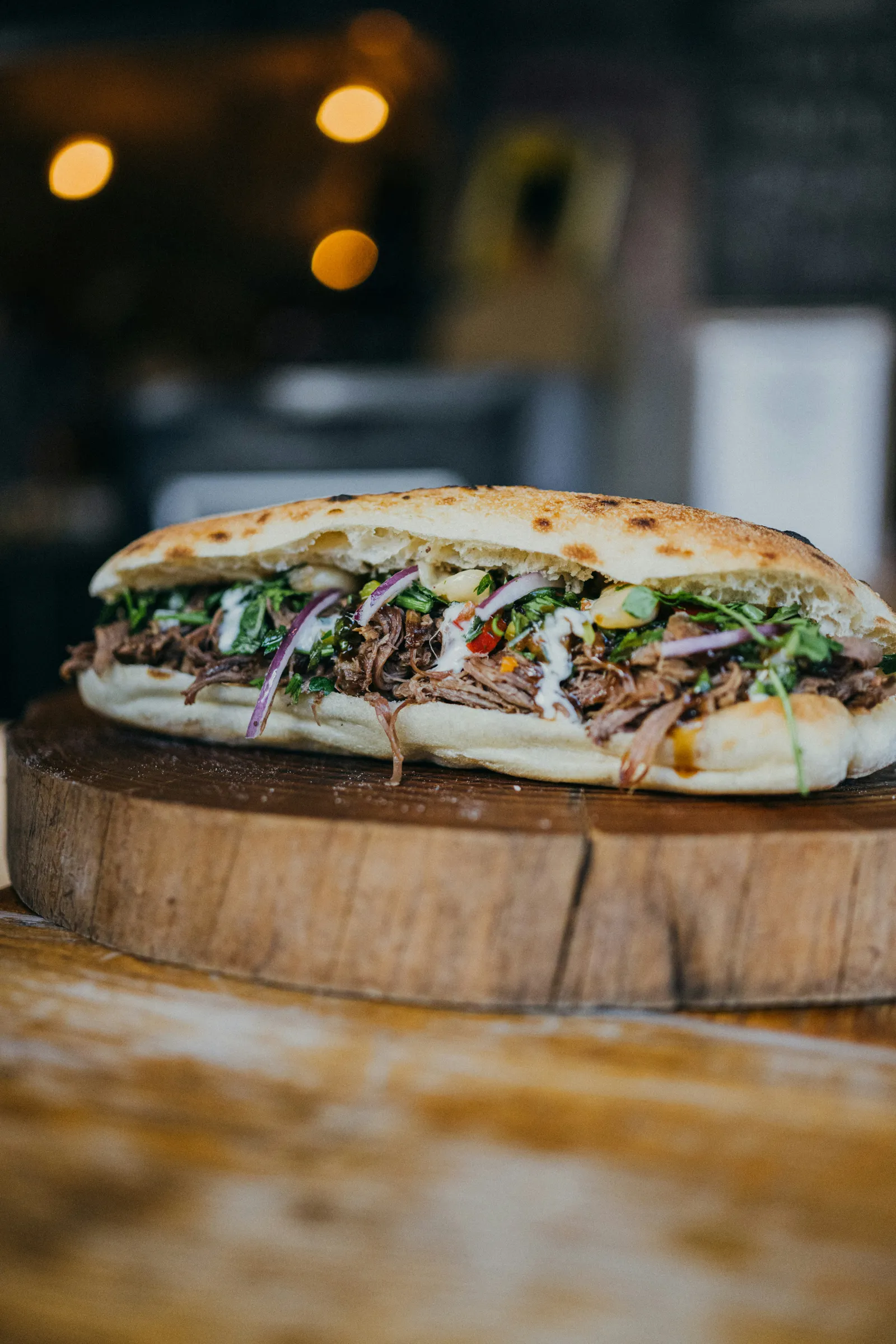 Döner im Fladenbrot auf einer Holzscheibe, dahinter warme Lichtpunkte im Dunkeln